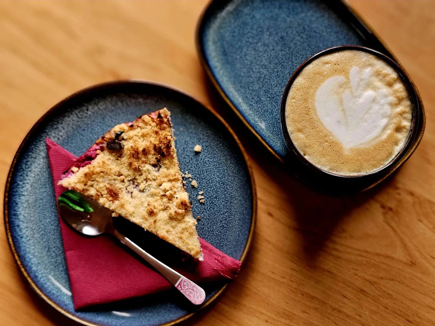 Kus domácího koláče s drobenkou a flat white na dřevěném stole